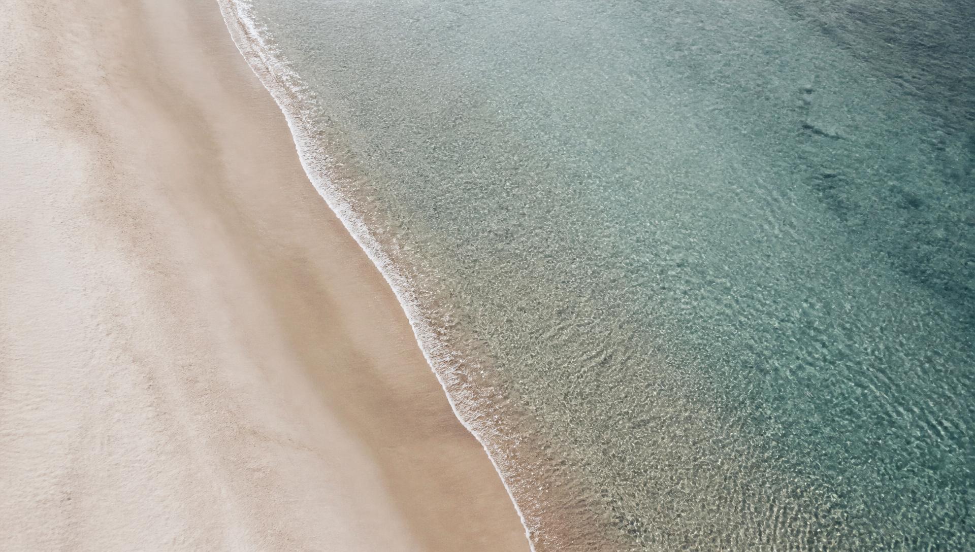Pale sand meeting clear blue-gray water from above